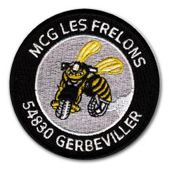 Ecusson rond brodé du moto club des Frelons. Au centre de l'écusson, sur fond gris, une abeille enfourchant une moto est brodée. Autour, sur un bandeau noir, on peut lire le texte MCG Les frelons, 54830 Gerbeviller.