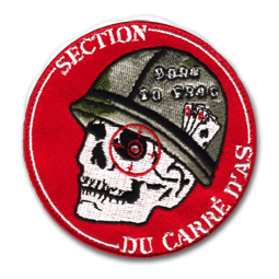 Ecusson rond brodé du club d'airsoft section du carré d'as. L'écusson a un fond rouge sur lequel est brodées une tête de mort portant un casque militaire. L'oeil de la tête de mort est cerclée de rouge, représentant un viseur.