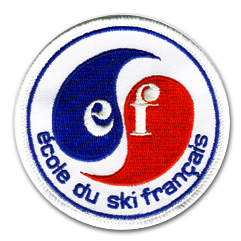 Ecusson rond brodé de l'école du ski français. Il représente deux arabesques rouges et bleues formant la lettre S au centre, avec les lettres E et F de part et d'autre. En dessous, en bleu sur fond blanc, le texte Ecole du ski français. Sur le bord , un fin liserai bleu.