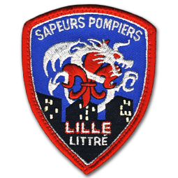 Ecusson brodé des pompiers de Lille littré. Il représente une fleur de lys rouge surmontée d'un dragon gris. le fond de l'écusson est bleu, et trois immeubles noires aux fenêtes allumées sont brodés sur la partie basse. En haut, le texte Sapeurs pompiers est écrit en gris, et en bas Lille Littré est écrit en gris et rouge. l'écusson a une forme de blason, et a une bordure rouge.